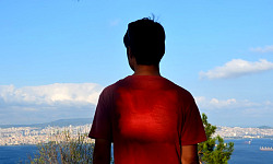 रोशनी बिखेरते हृदय वाला एक युवक एक शहर की ओर देखने वाली पहाड़ी पर खड़ा है