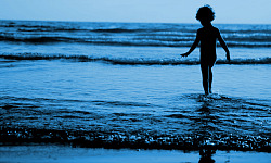 kleiner Junge steht im Wasser am Rande der plätschernden Wellen