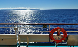 Blick vom Deck eines Schiffes über das Wasser, mit einem Lebensretter an der Reling