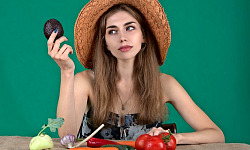 en kvinna med en mängd färska grönsaker framför sig och håller upp en avokado