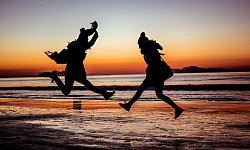 समुद्र तट पर दो लोग खुशी से उछल रहे हैं