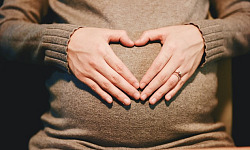 子宮の上でハートの形を作る女性の手