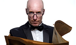 一個戴著領結、戴著老花眼鏡、手裡拿一份打開的報紙的男人