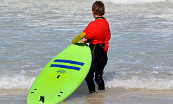 Ребенок стоит на берегу океана и держит в руках доску для серфинга