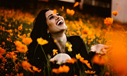 una mujer riendo en un campo de flores de color naranja brillante