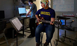 Jong man speel kitaar terwyl hy 'n helm dra wat bedek is met elektrodes wat breinaktiwiteit meet
