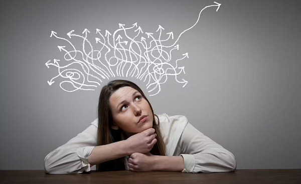 Girl thinking with arms resting on a table, arrows in different directions above her head