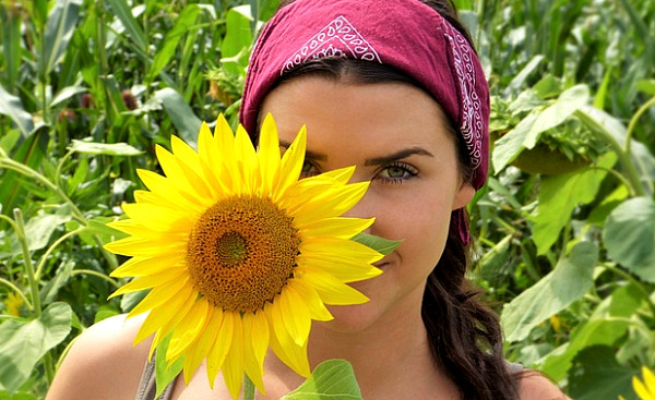 nainen seisoo hieman hänen päänsä kokoisen auringonkukan takana