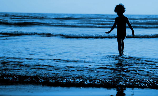 युवा लड़का पानी में उठती लहरों के किनारे खड़ा है