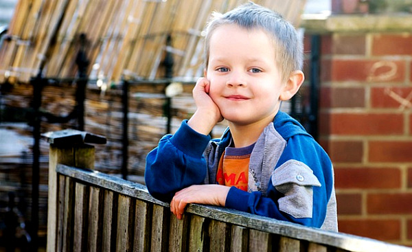 en ung pojke står vid ett staket och ser lugnt ut
