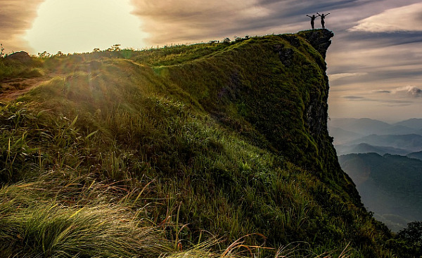 two people standing triumphantly on the edge of a cliff