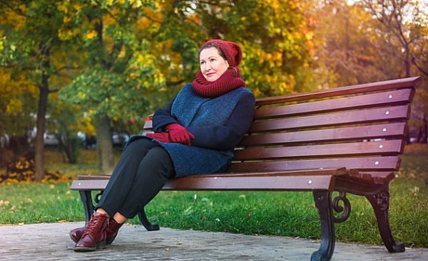 smilende kvinne sitter på en parkbenk på en høstdag