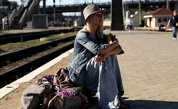鉄道駅でスーツケースの上に座っている女性