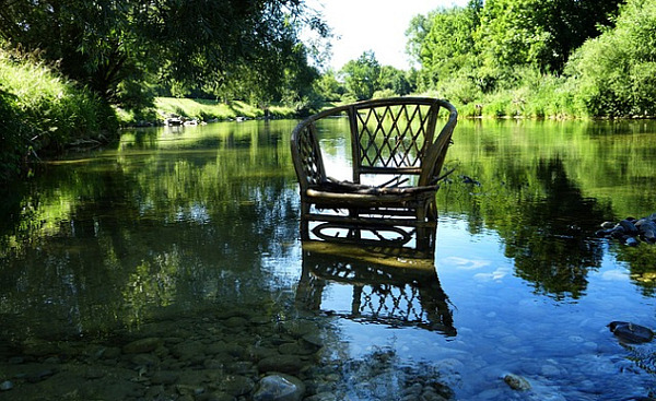 یک صندلی حصیری در آب های آرام رودخانه ای در نزدیکی ساحل رودخانه