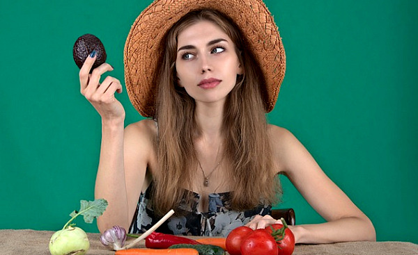 una donna con una serie di verdure fresche davanti a sé e con in mano un avocado