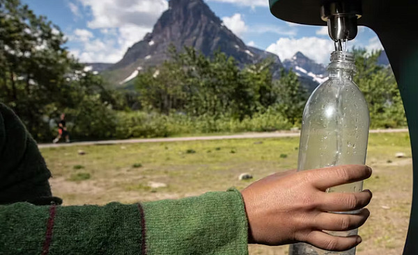 человек, наполняющий бутылку с питьевой водой из внешнего крана