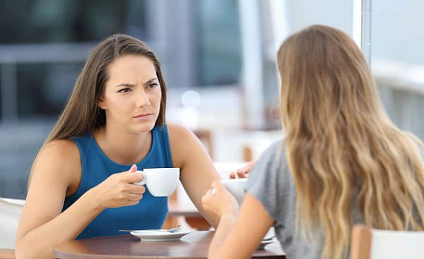 dua wanita menghadap antara satu sama lain sambil minum kopi