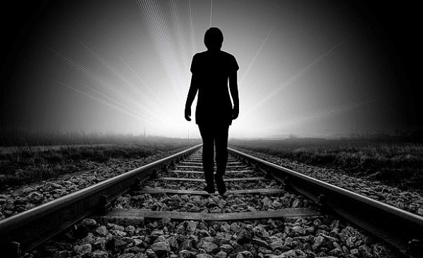 silhouette d'une personne marchant sur une voie ferrée vers la lumière