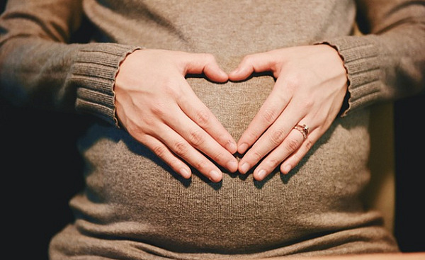 kvinnans händer bildar en hjärtform ovanpå hennes livmoder