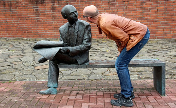 一個男人彎下腰仔細觀察長凳上的雕塑