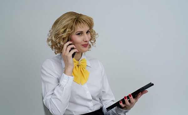 एक व्यवसायी महिला टैबलेट पकड़े हुए फोन पर बात कर रही है और हल्की सी मुस्कुरा रही है