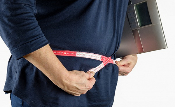 a person measuring themselves around the waist while holding a digital scale under their arm