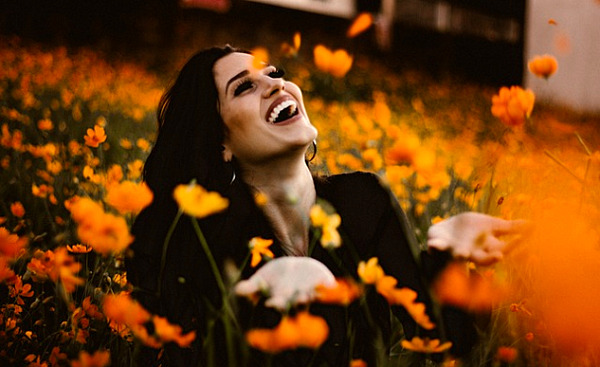 uma mulher rindo em um campo de flores laranjas brilhantes