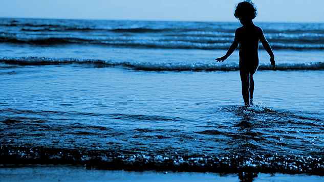 nuori poika seisoo vedessä sisään aaltoilevien aaltojen reunalla