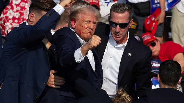 Trump with blood on his face holds up a clenched fist while people in suits surround him, illustrating the impact of social media on political violence.