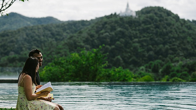 a couple sitting on the edge of a lake reading a book