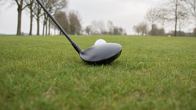 un primer plano de un palo de golf situado justo delante de una pelota de golf