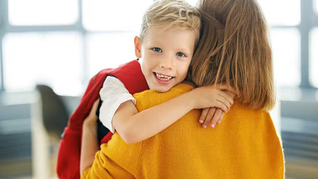 Child walking into school with backpack, smiling parent waving goodbye, representing a positive start to primary school.