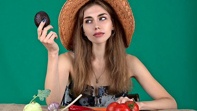 seorang wanita dengan pelbagai sayur-sayuran segar di hadapannya dan memegang alpukat