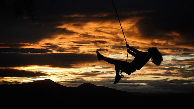 woman on a swing, happily swinging through the air. at sunset