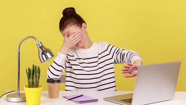 צעירה יושבת ליד שולחן מול קיר צהוב, מניחה יד אחת על עיניה ומשתמשת בשנייה כדי להגן על מסך המחשב שלה, ומציעה 'אני לא רוצה להסתכל על זה'.