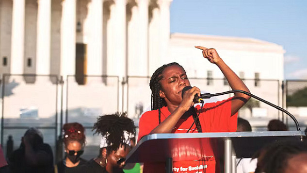 Racialized woman speaking at a protest, highlighting the challenges and backlash faced while advocating for social change.