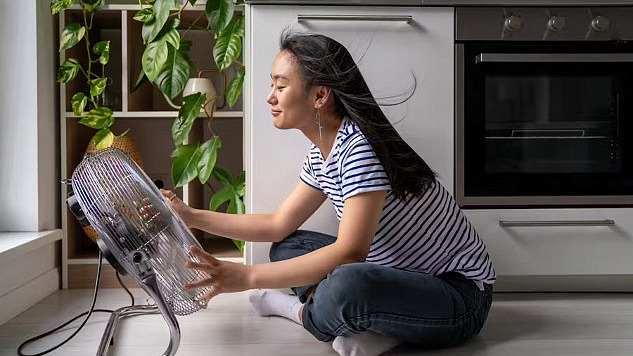 A young woman sitting close to a large electric fan. Not the most effective way to cool down