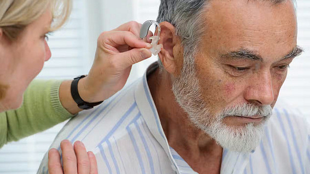 A doctor assists an older man with a hearing aid, a key tool in reducing dementia risk. Addressing modifiable risk factors like hearing loss can delay cognitive decline.