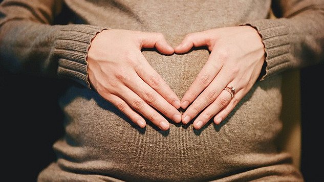 Las manos de una mujer formando un corazón encima de su útero.