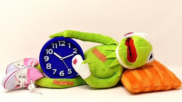 seekor katak yang sakit berbaring sambil memegang jam weker