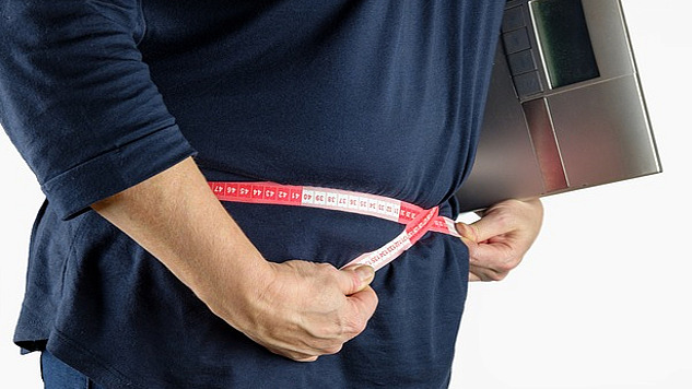 a person measuring themselves around the waist while holding a digital scale under their arm