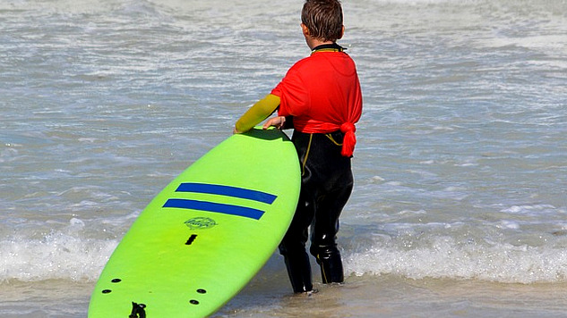 समुद्र के किनारे बॉडी सर्फिंग बोर्ड पकड़े खड़ा बच्चा