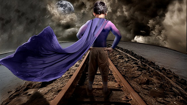 a young boy wearing a superpower cape standing on a railroad track