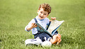 微笑的小男孩坐在外面，手裡拿著一本打開的書