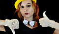 en ung kvinna klädd i fluga och ett clown ansikte med vita handskar som ger tummen upp och tummen ner