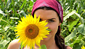 eine Frau, die leicht hinter einer sonnenblume steht, die so groß ist wie ihr Kopf