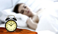 אישה ישנה עם שעון מעורר לא אלקטרוני בסגנון ישן על שידת הלילה
