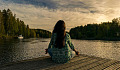 nainen, takaa katsottuna, istuu lootusasennossa laiturilla järven rannalla