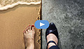 Split view of 2 feet: 1 barefoot on a beach, the other in black heels on a polished floor