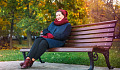 wanita tersenyum duduk di bangku taman pada hari musim gugur